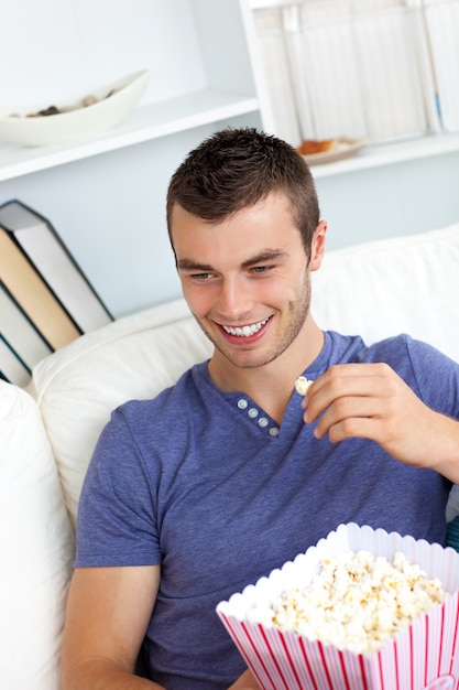 O homem atraente é relaxante na sala de estar com um controle remoto