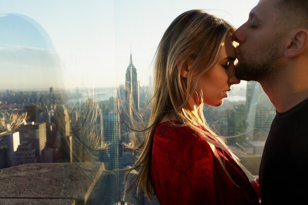 O homem beija a mulher tendem diante de uma ótima visão em Nova York atrás da janela