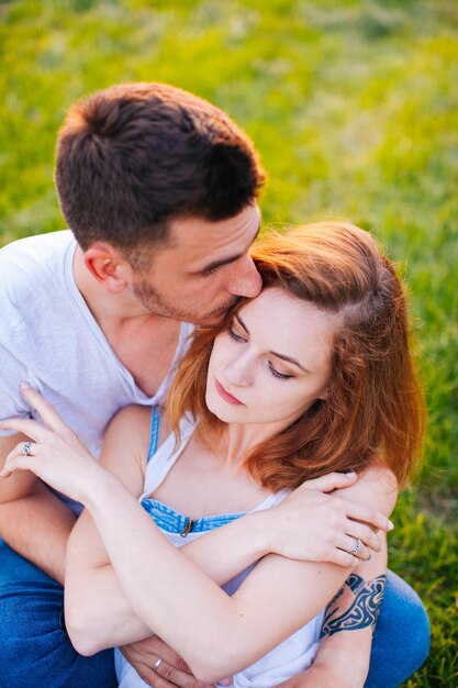 O homem bonito beija suavemente sua amada sentada na grama