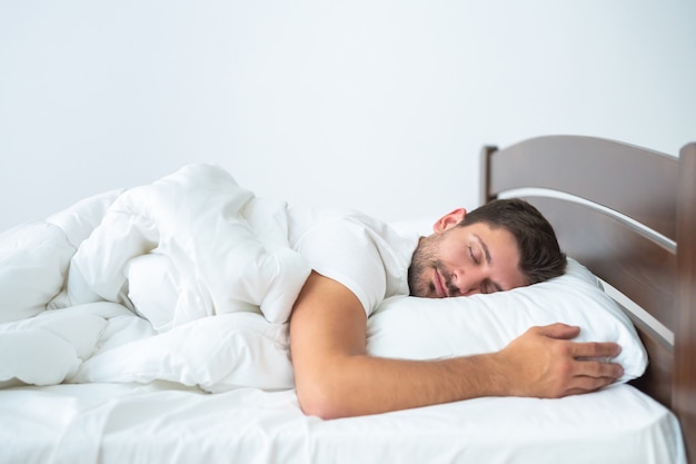 O homem bonito dormindo na cama no fundo branco