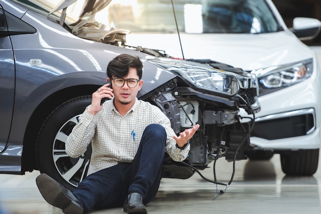 Foto o homem bonito fez um gesto estressante depois que o carro danificado foi atingido por um acidente e usou o telefone para pedir ajuda depois que o carro bateu na estrada - o carro tem seguro contra acidentes.