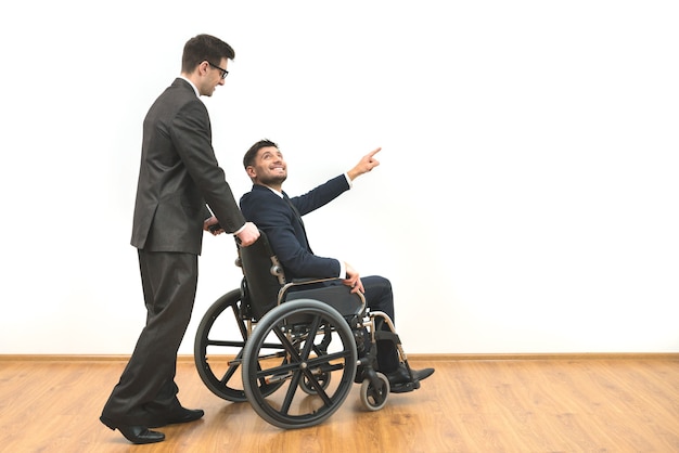 O homem carregando uma cadeira de rodas com deficiência no fundo da parede branca
