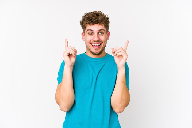 O homem caucasiano do cabelo encaracolado louro novo isolado indica com os dois dedos dianteiros que mostram acima um espaço em branco.