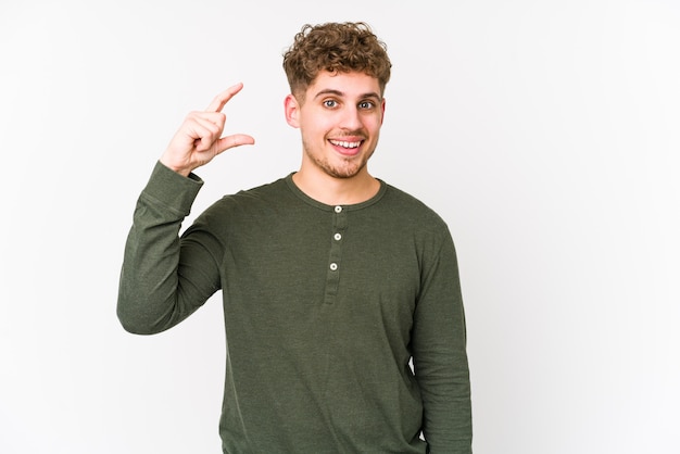 O homem caucasiano do cabelo encaracolado louro novo isolou guardar algo pouco com o dedo indicador, sorrindo e seguro.