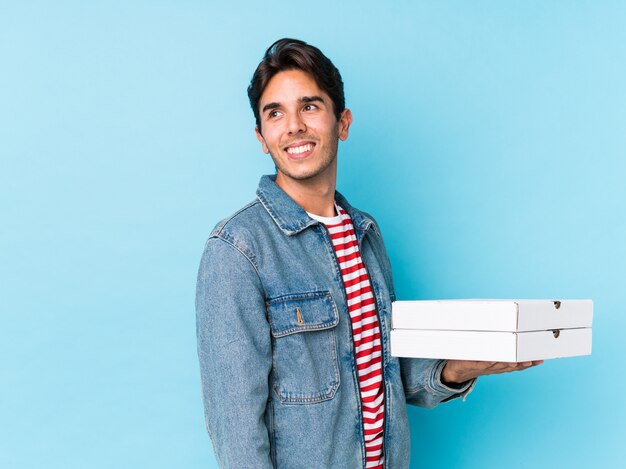 O homem caucasiano novo que mantém pizzas isoladas olha de lado o sorriso, alegre e agradável.