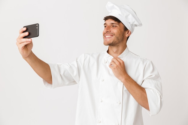 O homem chef isolado na parede branca tira uma selfie pelo celular.