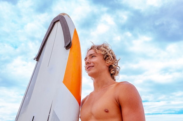 O homem considerável anda com prancha em branco branca espera a onda surfar o ponto na costa do oceano do mar. Conceito de esporte, fitness, liberdade, felicidade, nova vida moderna, hipster.