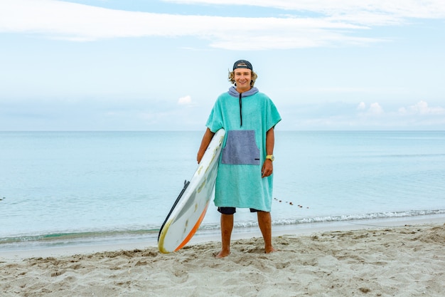 O homem considerável anda com prancha em branco branca espera a onda surfar o ponto na costa do oceano do mar.