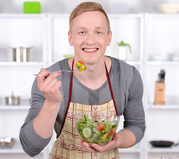 O homem considerável está provando a salada na cozinha.