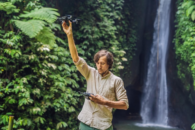 O homem controla o drone na perspectiva da floresta e da cachoeira