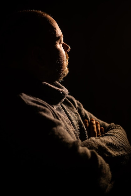 O homem cruzou as mãos em um suéter Silhueta de fundo escuro Meditação pensativa conceito de crise de meia-idade Um homem de meia-idade quarenta anos de idade