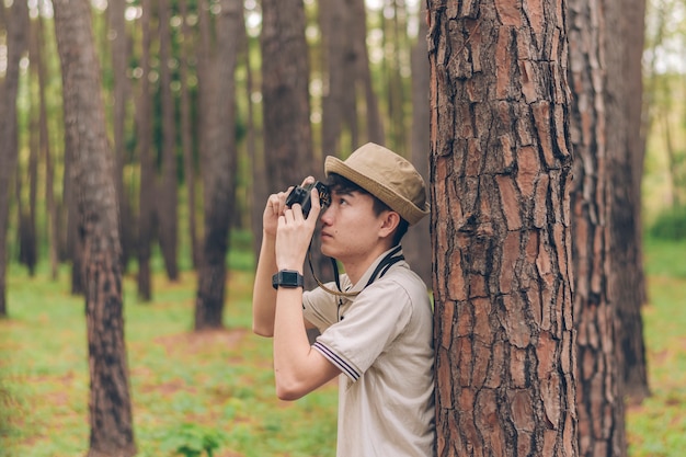 O homem da ásia veste camisa e chapéu está contra a árvore e tirando fotos na floresta