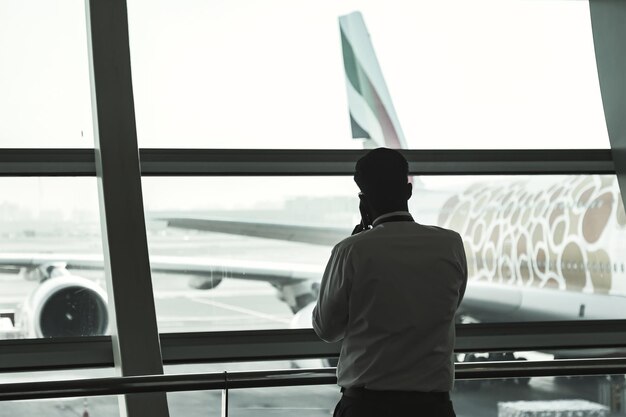 O homem da silhueta da vista traseira chama o telefone móvel sobre o fundo do aeroporto internacional do terminal da janela