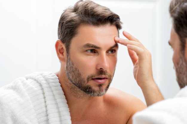 O homem de beleza caucasiano usa bálsamo facial hidratante para uma pele saudável conceito masculino de cuidados com a pele beleza masculina a