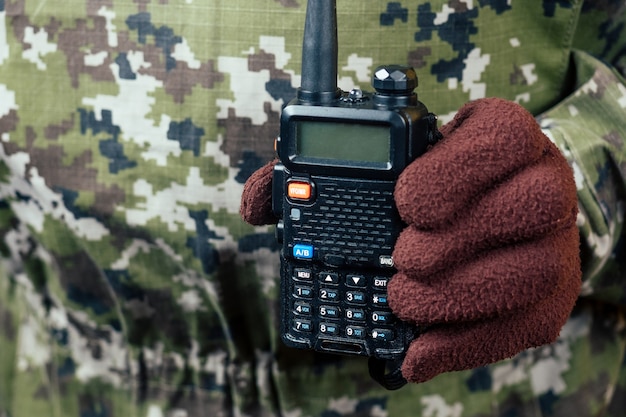 O homem de camuflagem e luvas está segurando o walkie-talkie na mão