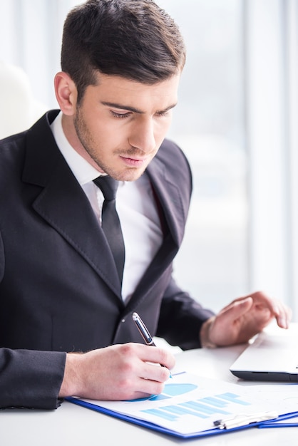 O homem de negócios concentrado está analisando gráficos em seu escritório.