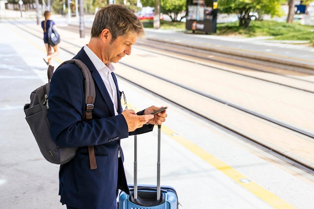 O homem de negócios que espera o trem verifica o horário no telefone