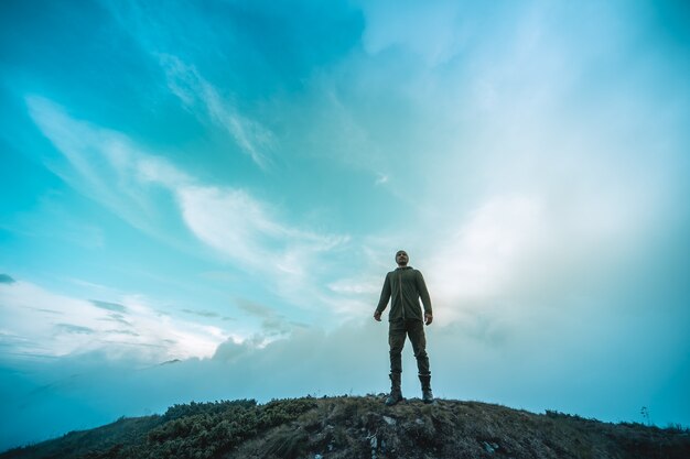 O homem de pé na montanha em um fundo de nuvens pitorescas