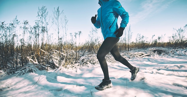 O homem de roupas esportivas está correndo pelas estradas rurais de inverno cobertas de neve