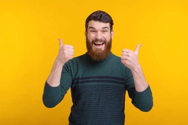 O homem de sorriso está aparecendo ambos os polegares no fundo amarelo.