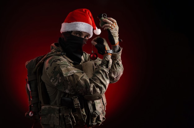 O homem de uniforme militar com uma arma e um chapéu de papai noel