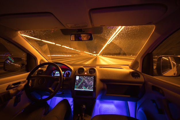 O homem dirige na estrada da chuva. Noite à noite. Vista interior