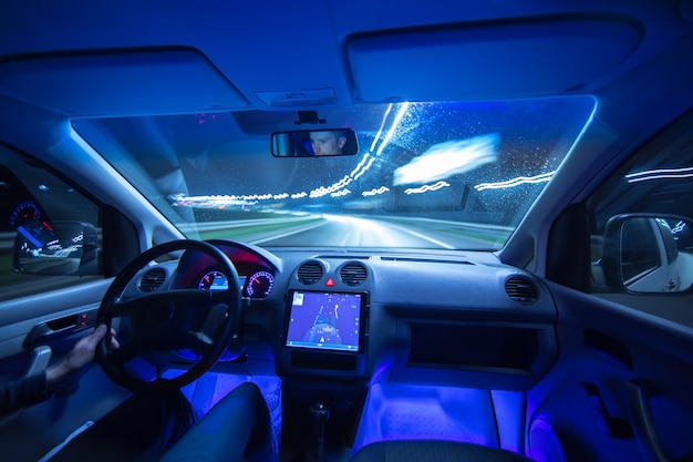 O homem dirige um carro com GPS na cidade à noite. Ângulo amplo