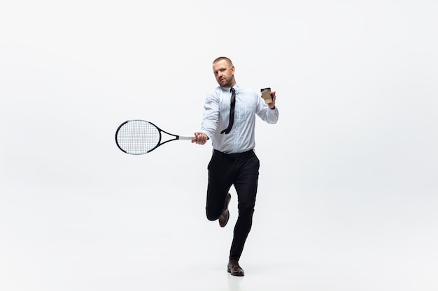 O homem do escritório joga tênis no fundo branco do estúdio, esportista
