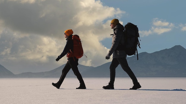 Foto o homem e a mulher com mochilas andando sobre um fundo de montanhas nevadas