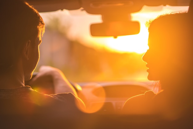 O homem e a mulher dirigem um carro no fundo do pôr do sol