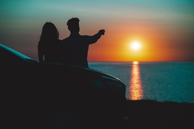 O homem e a mulher em pé perto do carro, no fundo da bela costa do mar