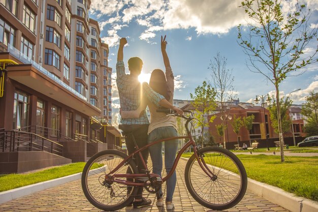 O homem e a mulher felizes em pé com uma bicicleta e gesticulando perto de um prédio