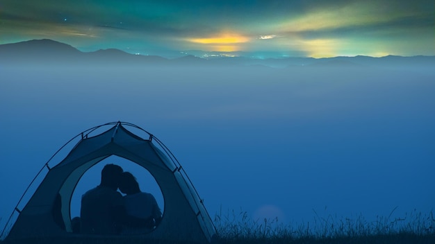 O homem e a mulher sentados na tenda do acampamento acima do fundo da cidade à noite