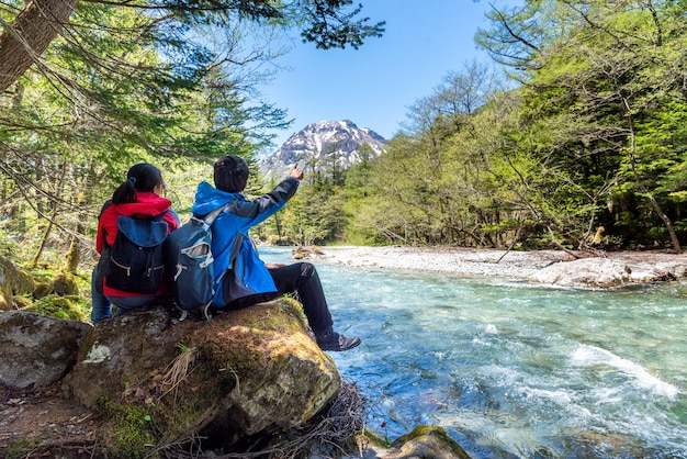O homem e a mulher sentam-se na rocha perto do rio de Azusa em Kamikochi em alpes do norte de Japão.