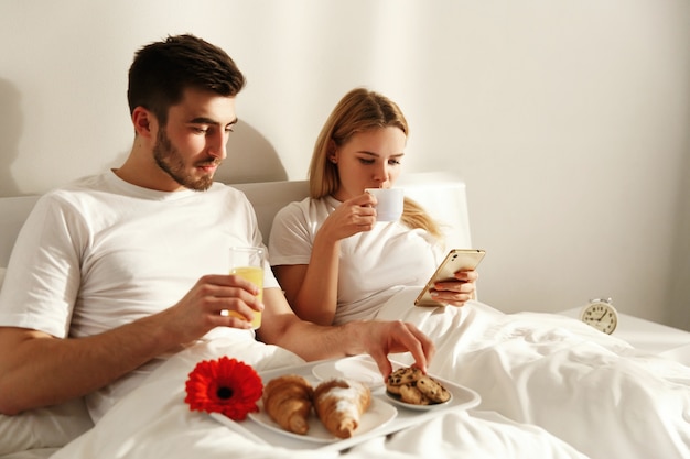 O homem e a mulher têm um delicioso café da manhã francês deitado na cama