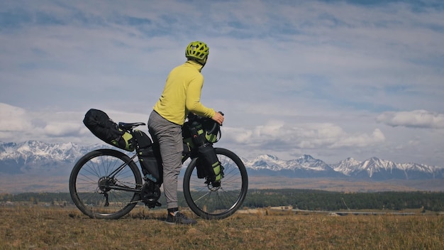 O homem e a mulher viajam em ciclismo de terreno misto com bikepacking As duas pessoas viajam com bolsas de bicicleta Sport bikepacking bike sportswear nas cores pretas verdes Montanhas cobertas de neve