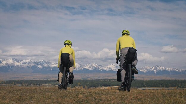 O homem e a mulher viajam em ciclismo de terreno misto com bikepacking As duas pessoas viajam com bolsas de bicicleta Sport bikepacking bike sportswear nas cores pretas verdes Montanhas cobertas de neve