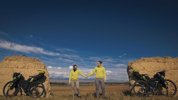 O homem e a mulher viajam em ciclismo de terreno misto com bikepacking As duas pessoas viajam com sacos de bicicleta Arco de pedra coberto de neve de montanha