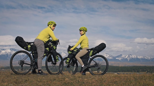 O homem e a mulher viajam em ciclismo de terreno misto com bikepacking As duas pessoas viajam com sacos de bicicleta Montanhas cobertas de neve