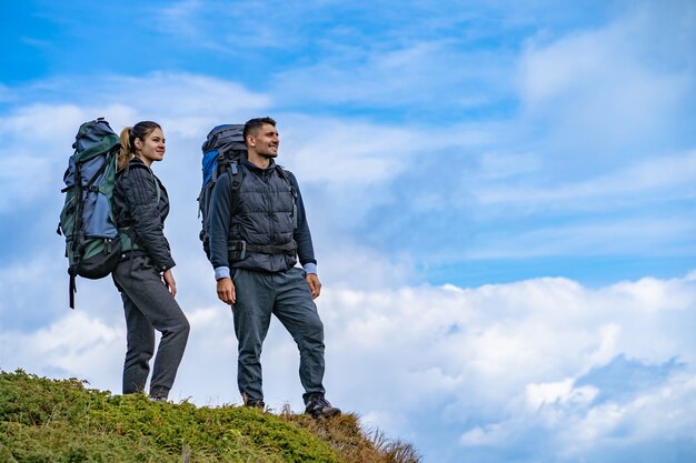 O homem e uma mulher com mochilas em pé no fundo da paisagem montanhosa