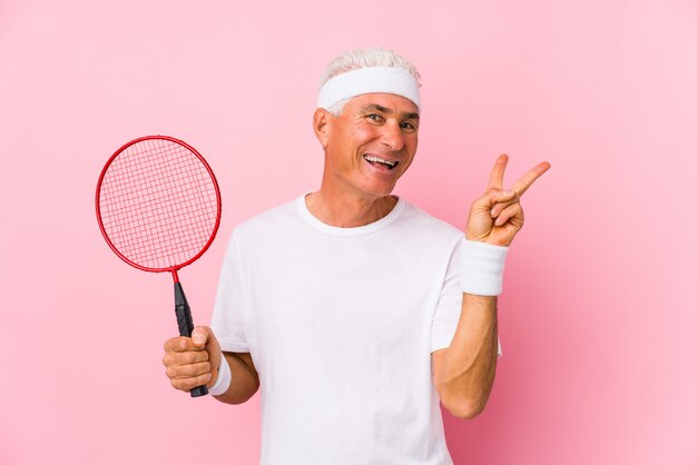 O homem envelhecido médio que joga o badminton isolou alegre e despreocupado mostrando um símbolo de paz com os dedos.