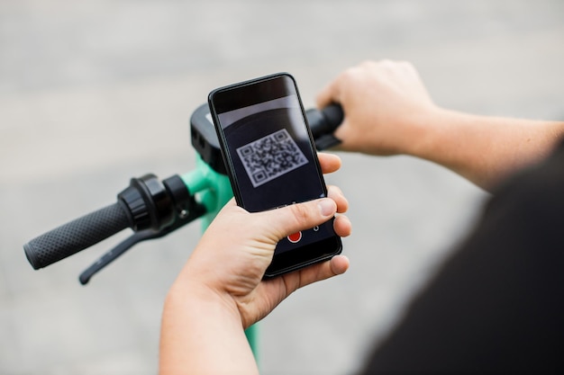 O homem escaneia o código QR pelo smartphone para desbloquear e alugar uma scooter elétrica na rua
