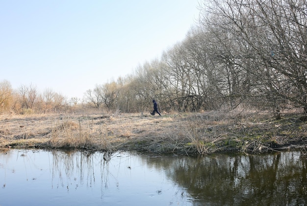 O homem está andando no campo seco com um saco de lixo nas mãos Poluição ambiental Árvores nuas e grama seca Natureza do rio