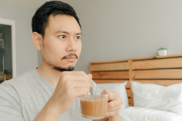 O homem está bebendo uma xícara de café na cama em seu quarto.