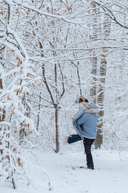 O homem está circulando a mulher em seus braços em uma floresta de neve