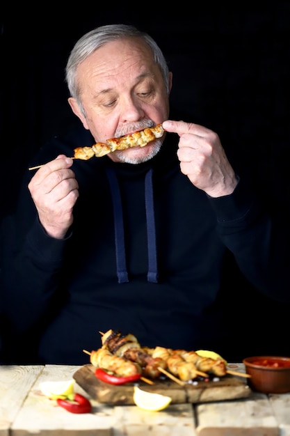 O homem esta comendo um espeto de frango