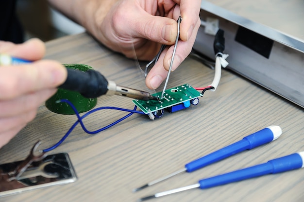 O homem está consertando a fonte de alimentação da lâmpada. Ele está segurando uma placa eletrônica e um ferro de solda.