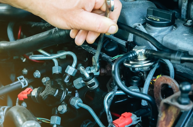 O homem está consertando um carro. Instrumentos nas mãos. Capô aberto do veículo.