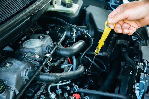 O homem está consertando um carro. Instrumentos nas mãos. Capô aberto do veículo.