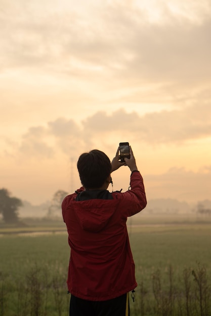 Foto o homem está fotografando uma bela paisagem de campo de arroz verde em uma manhã ensolarada
